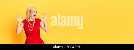 Porträt einer blonden Frau, die ein rotes Kleid trägt und schreit, mit Händen auf gelbem Hintergrund. Banner mit Kopierbereich. Banner mit Kopierbereich Stockfoto