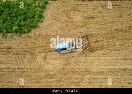 Castell'Arquato, Italien - April 2023 Landwirt, der auf gepflügtem, trockenem Feld einen Raupentraktor fährt, bevor er aus der Vogelperspektive sät Stockfoto