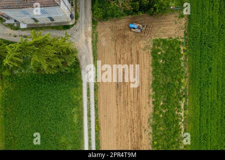 Castell'Arquato, Italien - April 2023 Landwirt, der auf gepflügtem, trockenem Feld einen Raupentraktor fährt, bevor er aus der Vogelperspektive sät Stockfoto