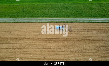 Castell'Arquato, Italien - April 2023 Landwirt, der auf gepflügtem, trockenem Feld einen Raupentraktor fährt, bevor er aus der Vogelperspektive sät Stockfoto