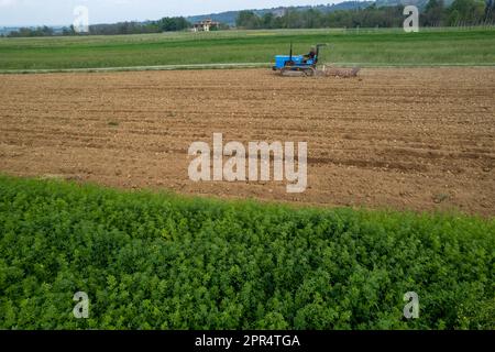 Castell'Arquato, Italien - April 2023 Landwirt, der auf gepflügtem, trockenem Feld einen Raupentraktor fährt, bevor er aus der Vogelperspektive sät Stockfoto