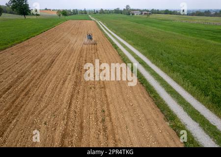 Castell'Arquato, Italien - April 2023 Landwirt, der auf gepflügtem, trockenem Feld einen Raupentraktor fährt, bevor er aus der Vogelperspektive sät Stockfoto