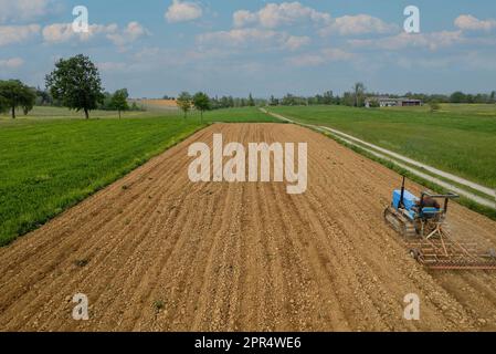 Castell'Arquato, Italien - April 2023 Landwirt, der auf gepflügtem, trockenem Feld einen Raupentraktor fährt, bevor er aus der Vogelperspektive sät Stockfoto