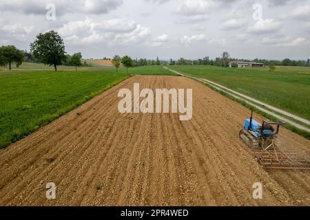 Castell'Arquato, Italien - April 2023 Landwirt, der auf gepflügtem, trockenem Feld einen Raupentraktor fährt, bevor er aus der Vogelperspektive sät Stockfoto