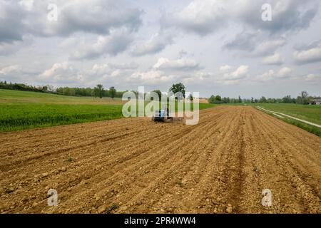 Castell'Arquato, Italien - April 2023 Landwirt, der auf gepflügtem, trockenem Feld einen Raupentraktor fährt, bevor er aus der Vogelperspektive sät Stockfoto