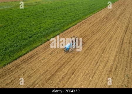 Castell'Arquato, Italien - April 2023 Landwirt, der auf gepflügtem, trockenem Feld einen Raupentraktor fährt, bevor er aus der Vogelperspektive sät Stockfoto