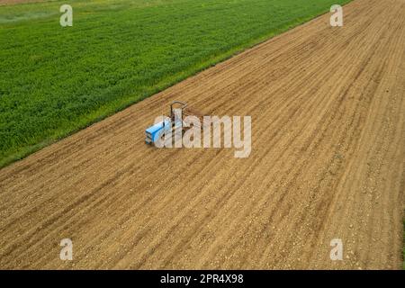 Castell'Arquato, Italien - April 2023 Landwirt, der auf gepflügtem, trockenem Feld einen Raupentraktor fährt, bevor er aus der Vogelperspektive sät Stockfoto