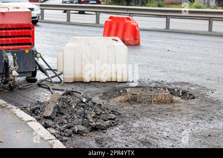 Ein pneumatischer Straßenkompressor mit Presslufthammer steht in der Nähe eines Kanalschachts, der auf der Straße einer Stadt repariert wird. Speicherplatz kopieren. Stockfoto