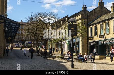 Menschen, die in der Sonne auf dem Platz vor dem Woolshops Einkaufszentrum sitzen, im Stadtzentrum, Halifax, West Yorkshire, Großbritannien Stockfoto