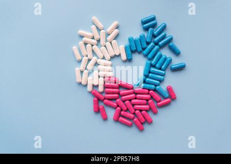 Verschiedene farbige Pillen - blau, rosa, weiß in Form eines Herzens, isoliert auf blauem Hintergrund. Platz für die Beschriftung Stockfoto