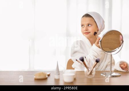 Süßes Kleines Mädchen, Das Make-Up Aufträgt, Während Es Zu Hause Am Frisiertisch Sitzt Stockfoto