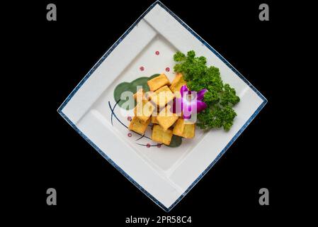 Vietnamesischer gebratener Tofu auf weißem Teller isoliert auf schwarzem Hintergrund für eine gute Sicht auf die Speisekarte Stockfoto