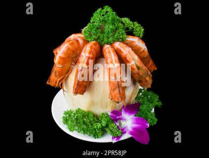 Orangengarnelen in der Kokosnuss mit Sauce isoliert auf schwarzem Hintergrund, Seitenansicht Stockfoto