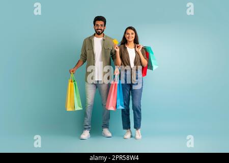 Fröhliche östliche Liebhaber mit Einkaufstaschen und Bankkarte Stockfoto