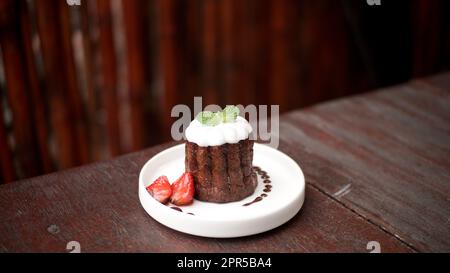 Caneles de bordeaux: Traditionelles französisches süßes Dessert mit Zucker oder weißer glasierter Schokolade und Erdbeergarnierung Stockfoto