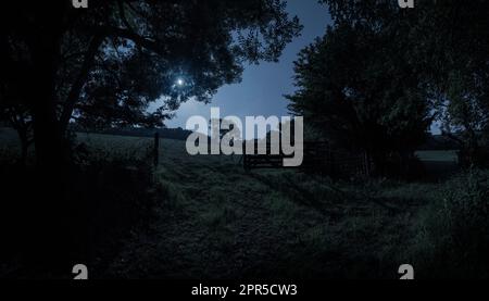 Ein Tor auf einer Landstraße auf dem Ackerland in Cornwall, England, beleuchtet vom Glanz des Vollmondes. Mondlicht auf der Landschaft der Eidechsenhalbinsel. Stockfoto