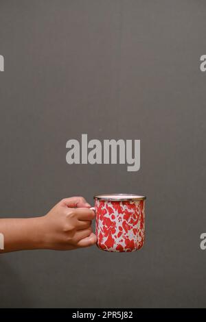 Porträt- oder vertikale Aufnahme einer handgeführten Emaille-Tasse auf dunkelgrauem Hintergrund Stockfoto