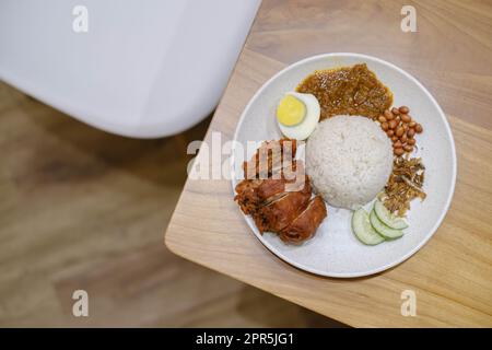 Flach liegend oder Draufsicht eines Tellers Nasi Lemak mit knusprigem Huhn, Ei, Erdnüssen, Lemak-Sauce und Sardellenfisch Stockfoto