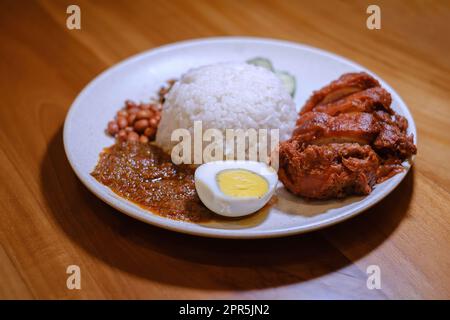 Ein Teller Nasi Lemak mit knusprigem Hähnchen, Ei, Erdnüssen, Lemak-Sauce und Sardellenfisch mit verschwommenem Hintergrund Stockfoto