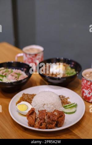 Porträt oder vertikales Bild einer malaysischen Küche enthielt gedünsteten Hühnerreis, Nasi Lemak, Chili Pan Mee und zwei Tassen Thai-Tee auf einem Woode Stockfoto