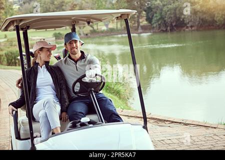 Genießen Sie einen schönen Tag auf dem Grün. Ein lächelndes junges Paar, das in einem Wagen auf einem Golfplatz sitzt. Stockfoto