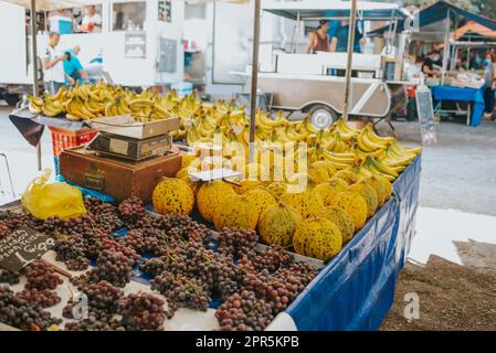 Tisch mit türkischen Alacati-Melonen neben Trauben und Bananen auf einem europäischen Bauernmarkt in Athen, Griechenland Stockfoto