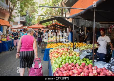 Frau geht an einem Äpfelstand auf einem europäischen Bauernmarkt in Athen vorbei, während der Verkäufer in die Kamera schaut Stockfoto