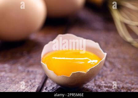Zerbrochenes Hühnerei, sichtbares Eigelb auf Holztisch, Kochen mit Bio-Eiern Stockfoto