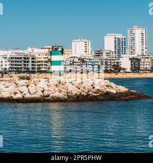 Quarteira, Portugal - 24. April 2023: Blick auf den farbenfrohen Leuchtturm mit Quarteira im Hintergrund, Algarve, Portugal Stockfoto