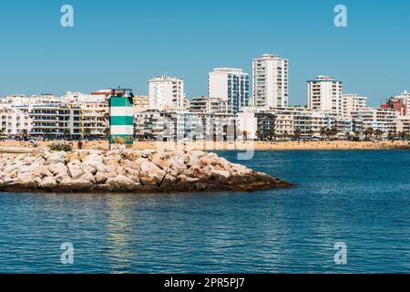 Quarteira, Portugal - 24. April 2023: Blick auf den farbenfrohen Leuchtturm mit Quarteira im Hintergrund, Algarve, Portugal Stockfoto