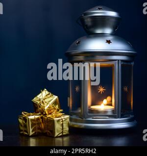 Weihnachtskarte: Laterne mit Kerzen, leuchtend glänzende Schachteln mit Geschenken auf dunkelblauem Hintergrund. Stockfoto