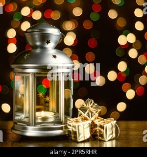 Weihnachtskarte: Eine Laterne mit Kerzen, helle, glänzende Schachteln mit Geschenken und verschwommene Lichter im Hintergrund. Stockfoto