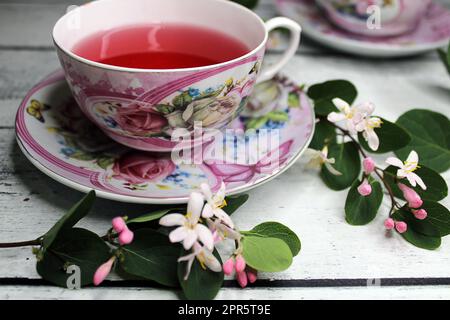 Eine Tasse Tee auf einem Holztisch mit weißem und pinkfarbenem Blumenhintergrund Stockfoto