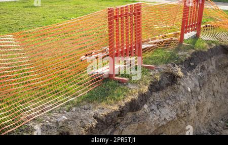 Schutzzaun am Rand des Grabens während der Reparaturarbeiten von unterirdischen Versorgungsunternehmen. Nahaufnahme, Sommer, im Freien Stockfoto