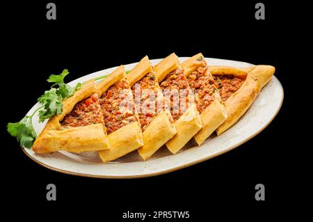 türkische Pizza Pide mit Hackfleisch liegt auf einem Teller auf einem schwarzen isolierten Hintergrund Stockfoto