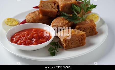 Jachnun oder Jahnun, jüdisches Gebäck aus dem jemenitischen Raum, serviert mit frischer geriebener Tomate und gekochtem Ei und Zhug, die von den Adeni-Juden stammen, und traditionell serviert am Sabbat-Morgen in Israel. Stockfoto