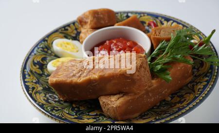 Jachnun oder Jahnun, jüdisches Gebäck aus dem jemenitischen Raum, serviert mit frischer geriebener Tomate und gekochtem Ei und Zhug, die von den Adeni-Juden stammen, und traditionell serviert am Sabbat-Morgen in Israel. Stockfoto