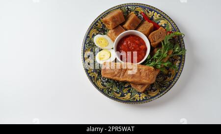 Jachnun oder Jahnun, jüdisches Gebäck aus dem jemenitischen Raum, serviert mit frischer geriebener Tomate und gekochtem Ei und Zhug, die von den Adeni-Juden stammen, und traditionell serviert am Sabbat-Morgen in Israel. Stockfoto