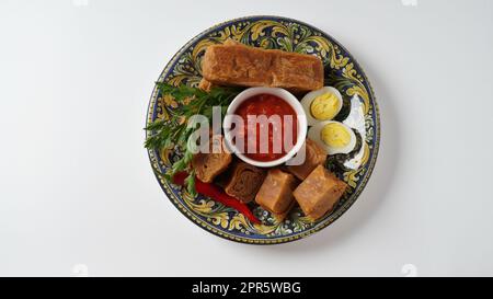 Jachnun oder Jahnun, jüdisches Gebäck aus dem jemenitischen Raum, serviert mit frischer geriebener Tomate und gekochtem Ei und Zhug, die von den Adeni-Juden stammen, und traditionell serviert am Sabbat-Morgen in Israel. Stockfoto