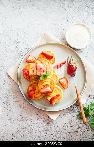 Hüttenkäse-Pfannkuchen, Ricotta-Fritters oder Syrniki mit Minze und Erdbeeren. Gesundes und köstliches Frühstück am Morgen. Stockfoto