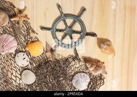 Captains Wheel mit Fischernetz und Meeresmuscheln auf Holzhintergrund Stockfoto