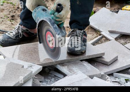 Ein Arbeiter mit einer Kreissäge schneidet in Nahaufnahme eine Fliese. Stockfoto