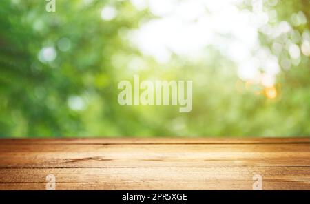 Leere leere Holzbohle, Terrasse oder Tisch mit unscharfen grünen Bäumen im Hintergrund Stockfoto