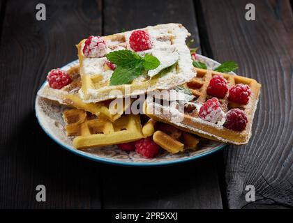 Stapel gebackene belgische Waffeln mit reifen roten Himbeeren, bestreut mit Puderzucker Stockfoto