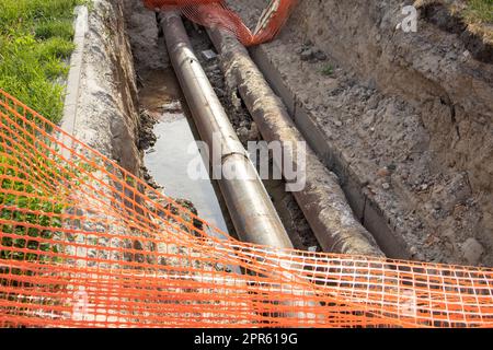 Reparatur der Heizungsanlage durch Verlegung neuer unterirdischer Metallrohre im Graben. Rekonstruktion des Stadtheizungssystems. Maschendrahtzaun für Arbeitssicherheit Stockfoto