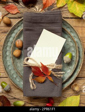 Rustikale Tischdekoration im Herbst mit leerer Platzkarte zwischen bunten Blättern und Beeren, Draufsicht, Modell Stockfoto