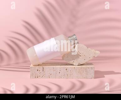 Kosmetikflasche mit leerem Etikett liegt auf Stein auf hellrosa, Palmblatt harter Schatten dahinter, Nahaufnahme, Mockup. Hautpflegeprodukt. Naturkosmetik Stockfoto
