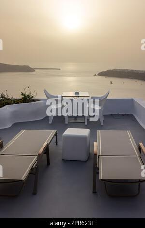 Sonnenliegen und Stühle auf der Terrasse im Dorf Imerovigli mit herrlichem Blick auf den Sonnenuntergang über der Caldera in Santorin Stockfoto