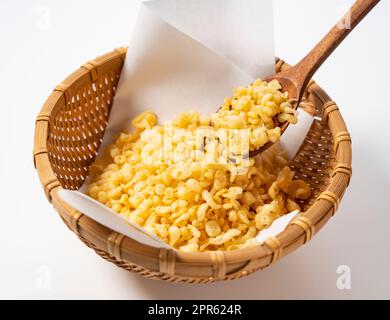 Tempura Dregs, serviert in einem Sieb auf weißem Hintergrund mit einem Holzlöffel. Stockfoto