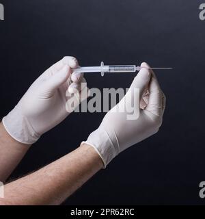 Mit Handschuhen gehaltene Hände, die eine Spritze halten Stockfoto